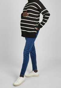 Randig svart och vit tröja med en lös passform, i kombination med blå skinny jeans och vita sneakers. Tröjan har ribbade muddar och nederkant.