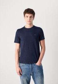 Tricou de culoare bleumarin, cu mânecă scurtă, având un decolteu rotund și un detaliu discret cu logo pe piept, fabricat din material moale din bumbac.