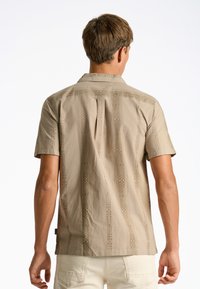 Korte mouwen tan shirt gemaakt van stof met een textuur, geometrisch patroon. Heeft een klassieke kraag en subtiele details aan de achterkant.