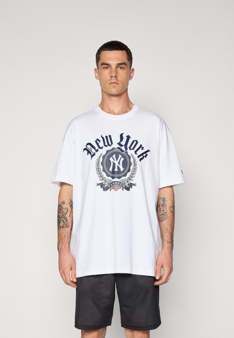 Camiseta de algodón blanca con un gráfico en azul marino que dice "New York", con un emblema y detalles florales, combinada con pantalones cortos de malla negros.