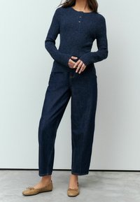 Haut en maille bleu foncé avec un motif texturé, doté d'un col rond et d'une patte de boutonnage à trois boutons, associé à un pantalon en denim foncé ample.