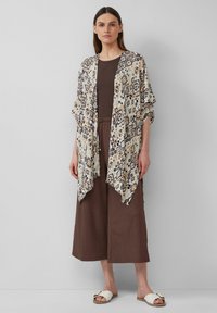 Geprinte kimono-stijl cardigan met geometrische patronen in beige, bruin en marineblauw; gecombineerd met een bruin ribbeltop en wijde broek.