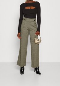 Haut noir à manches longues avec une découpe, associé à un pantalon taille haute à jambes larges avec un motif pied-de-poule et des boutons décoratifs à l'avant.