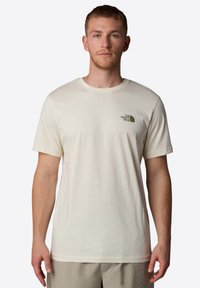 Beige bomuld t-shirt med korte ærmer og rund udskæring, med et grønt logo på venstre bryst og en glat tekstur.