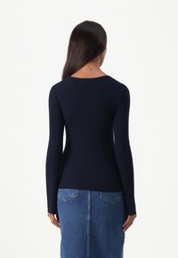 Pull en maille côtelée marine à manches longues avec un col rond. Associé à une jupe en denim comportant deux poches arrière et une silhouette ajustée.