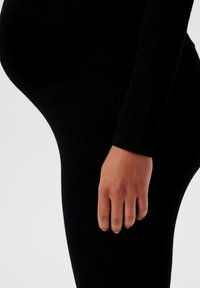 Leggings noirs en tissu extensible, dotés d'une coupe ajustée qui épouse le corps. La texture semble lisse avec un léger éclat.