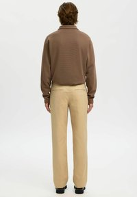 Brun långärmad skjorta med krage, kombinerad med beige byxor med raka ben. Outfitten har en enkel, diskret design och en mjuk textur.