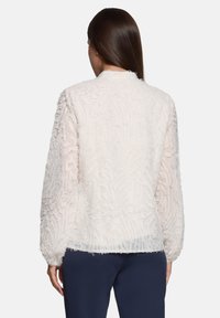 Hellrosa strukturierte Jacke mit weichem, flauschigem Aussehen. Verfügt über lange Ärmel und einen geraden Saum. Auf der Rückseite sind keine Verschlüsse sichtbar.