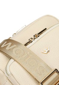 Borsa in finta pelle beige con zip dorata, tracolla regolabile con logo e dettaglio texture sottile sulla superficie.