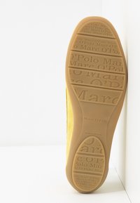 Semelle de chaussure en daim jaune avec un logo moulé et un design texturé. Présente des bords lisses et une base en caoutchouc brun clair.