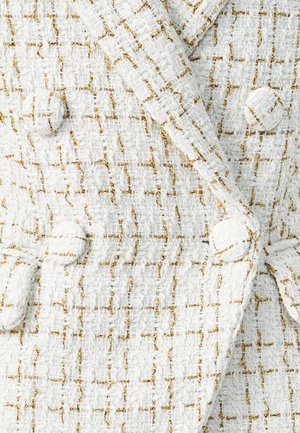 Bela teksturirana tkanina z zlatim nitmi, ki vsebuje dvorekli obliko in okrogle gumbe.