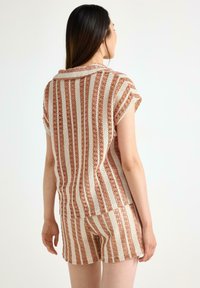 Stickad tvådelad outfit med horisontella ränder i rost- och krämfärger. Toppen har korta ärmar och shortsen är figurnära.