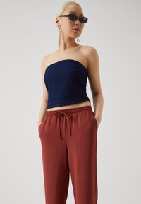 Strapless dark blue top in textured fabric, paired with loose, rust-colored pants featuring an elastic waistband and side pockets.