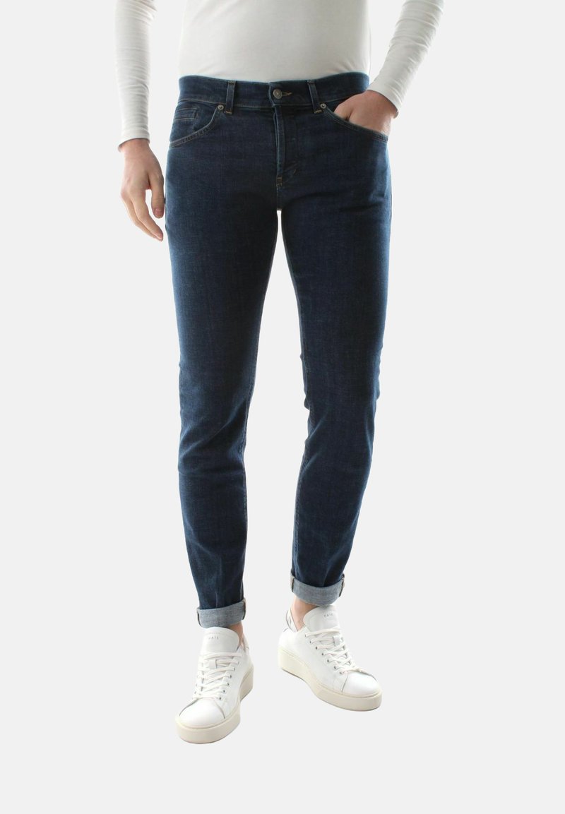 Jeans in denim blu scuro con vestibilità slim, dotati di tasche frontali e orli arrotolati. Abbinati a sneakers bianche per un look casual.