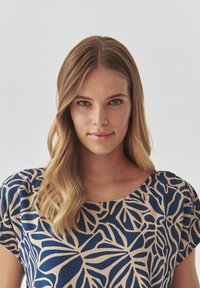 Mørkeblå og beige kortærmet bluse med bladmønster. Stoffet ser glat ud med en afslappet pasform og bred halsudskæring.