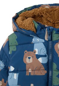 Chaqueta azul acolchada con ilustraciones de animales y árboles. Presenta un forro marrón suave, capucha y cremallera frontal. Textura suave y diseño colorido.