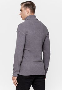 Szary sweter z golfem, prążkowany, z długimi rękawami, dopasowanym krojem i lekko podwiniętym kołnierzem, w zestawie z czarnymi spodniami.