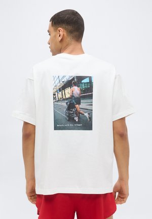 Man in white shirt with photo of runner pushing stroller on back, caption reads "Runners, we're still different."