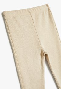 Leggings beige con un sutil patrón de espiga, hechos de una tela suave y elástica. Cuentan con una cinturilla elástica y sin costuras visibles.