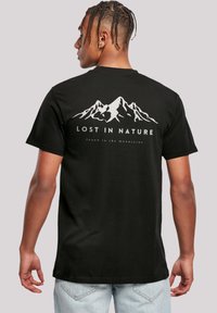 Schwarzes T-Shirt mit einem weißen Bergmotiv und dem Text "VERLOREN IN DER NATUR" sowie "gefunden in den Bergen" darunter. Kurzärmlig, lässige Passform.