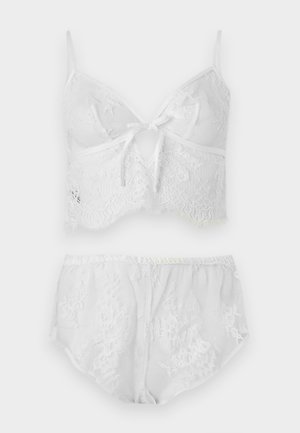 Σετ λευκά δαντελωτά εσώρουχα με κορσέ cropped που διαθέτει φιόγκο μπροστά και αντίστοιχα δαντελωτά κοντά σορτς με ψηλή μέση.