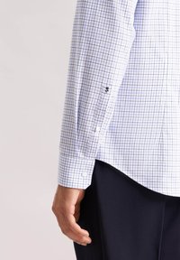Camicia a scacchi blu e bianca con polsino abbottonato e logo ricamato sulla manica. Tessuto di cotone morbido, vestibilità sagomata, bottoni a contrasto.