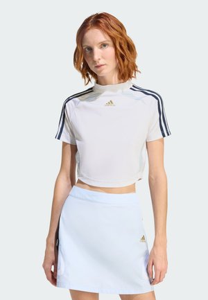 Biały krótki sportowy top z niebieskimi akcentami i złotym logo Adidas, zestawiony z jasnoniebieską spódnicą z bocznymi kieszeniami i gładką teksturą.