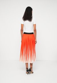 Folyékony redős szoknya élénk narancssárga és fehér színátmenettel, fekete derékkal. Fekete magassarkú szandálokkal párosítva.