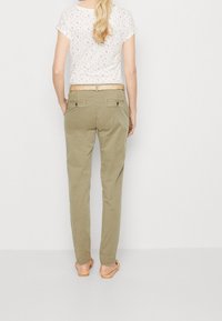 Lehká krémová květinová blůza s ohrnutými rukávy, v kombinaci s olivově zelenými chinos kalhotami s zadními kapsami a tkaným opaskem.