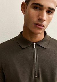 Polo shirt verde scuro con colletto con zip; presenta una superficie liscia e un design pulito e minimale che mette in risalto il dettaglio della zip.