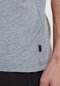 Gray cotton t-shirt featuring a stitched hem, side seam, and a small black brand tag near the hemline. Smooth texture, casual design.