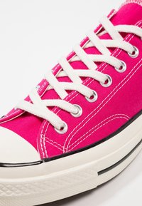 Baskets en toile rose avec lacets blancs, embout en caoutchouc et semelle extérieure en caoutchouc noir. Présente des œillets en métal argenté et des détails de couture blanche.