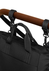 Fekete anyagú táska két felső fogantyúval, állítható pántokkal és rögzítőhoroggal, egy texturált barna babakocsi fogantyún pihen.