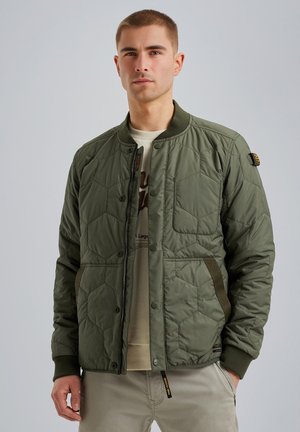 Olive green quilted bomber jacket with snap fasteners, ribbed cuffs, side pockets, and padded texture. Underneath, a light-colored shirt is visible.
