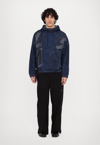 Sweat à capuche marine avec motif texturé et lettrage graphique, associé à un pantalon noir à jambes larges et des chaussures noires. Style décontracté, coupe confortable.