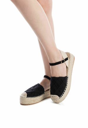 Espadrilles negras tejidas con suela de yute natural, que presentan una correa negra para el tobillo y un acabado texturizado en la parte superior.