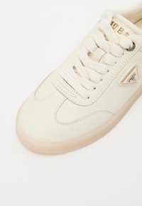 Vita lädersneakers med en texturerad yta, rund tå och krämfärgade snören. Har en logotyp i guldton och en beige gummisula.