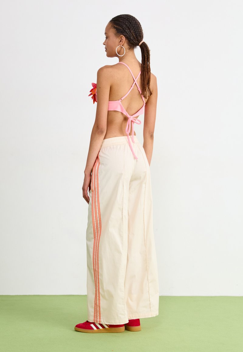 Różowy bikini bez pleców z krzyżującymi się ramiączkami, zestawione z kremowymi spodniami o szerokich nogawkach z pomarańczowymi paskami po bokach. Czerwone trampki dopełniają stylizację.