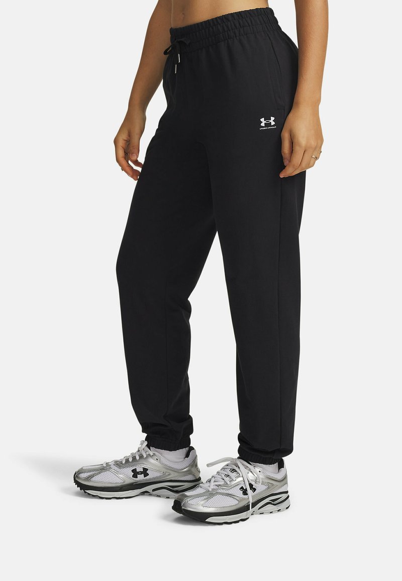 Pantaloni jogger neri con vita elastica e coulisse, con un piccolo logo bianco. Abbinati a scarpe da ginnastica argentate.