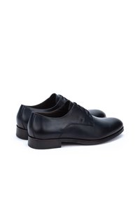Scarpe da uomo in pelle nera con finitura liscia, punta rotonda, design con lacci e tacco basso impilato. Dettagli minimalisti, nessun logo visibile.