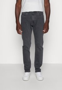 Tumedates hallid teksad slim-fit lõikes, valmistatud denimist, hõlmavad viit taskut ja peent õmblemist. Kombineeritud valgete spordijalgadega kontrasti saavutamiseks.