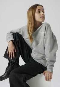 Felpa grigia con la scritta "Ispirato a Bowie", abbinata a jeans neri a gamba larga e stivali neri con lacci. Tessuto morbido e vestibilità rilassata.