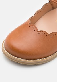 Brązowy skórzany but z falbaniastym brzegiem, gładką powierzchnią, okrągłym noskiem i jasną podeszwą podkreśloną detalami w postaci stężeń.