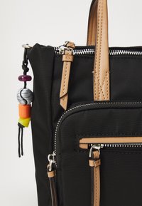 Black fabric backpack featuring tan leather accents, multiple zippered compartments, and colorful bead details on a decorative cord.