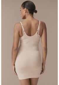 Beige shapewear kledingstuk met dunne verstelbare bandjes, een gladde textuur en een aansluitende silhoutte. Ontworpen om een naadloze uitstraling te bieden.