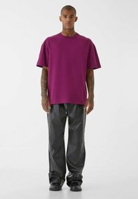 Fialové oversized tričko s krátkymi rukávmi v kombinácii s lesklými čiernymi širokými nohavicami. Hladká látka bez viditeľných vzorov alebo log.