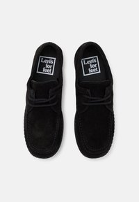 Mocassins en daim noir avec un bout rond, des lacets et une semelle en caoutchouc texturée. Étiquette "Levi's for feet" sur la semelle intérieure.