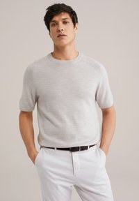 Suéter de punto de manga corta en gris claro con escote redondo y una textura sutil, combinado con pantalones blancos y un cinturón de trenzado negro.