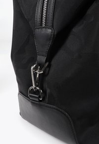 Svart väska med en strukturerad yta, med dragkedja och metalldetalj som lås. Släta läderdetaljer förbättrar dess moderna design.