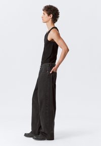 Top negro sin mangas y pantalones vaqueros de pierna ancha negros, que presentan una tela texturizada, un corte relajado y costuras notables. Combinados con calzado negro.
